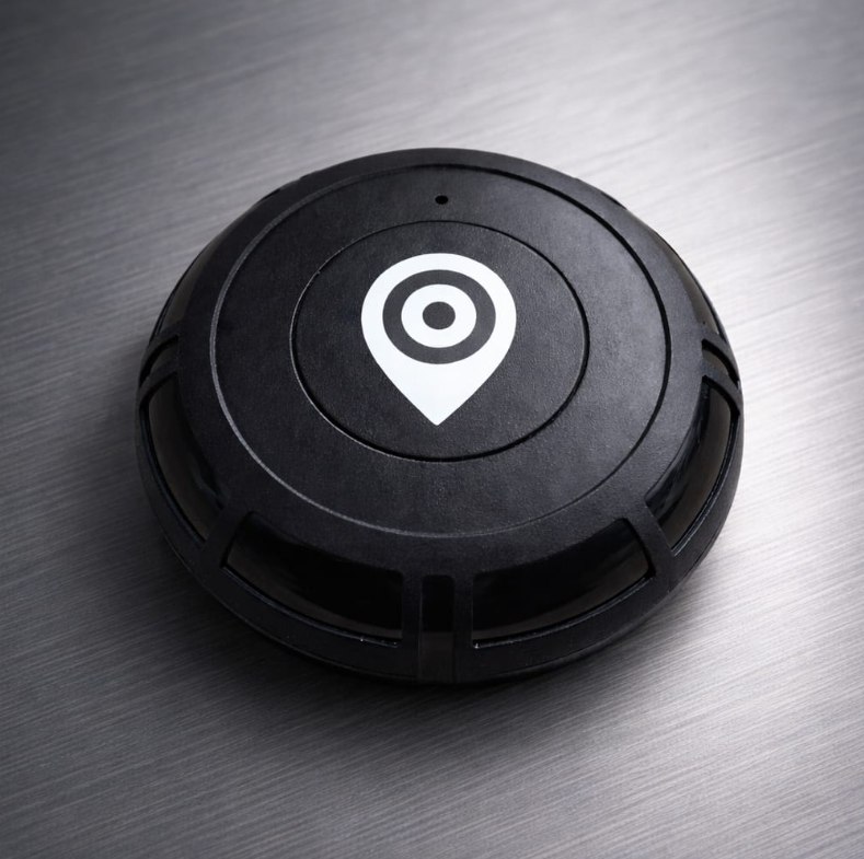 TAG de rastreamento da Argos, um disco preto com o ícone de localização, sobre superfície metálica escovada